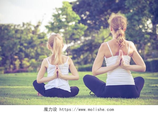 妈妈和女儿在公园的草地上做瑜伽练习双人瑜伽户外瑜伽